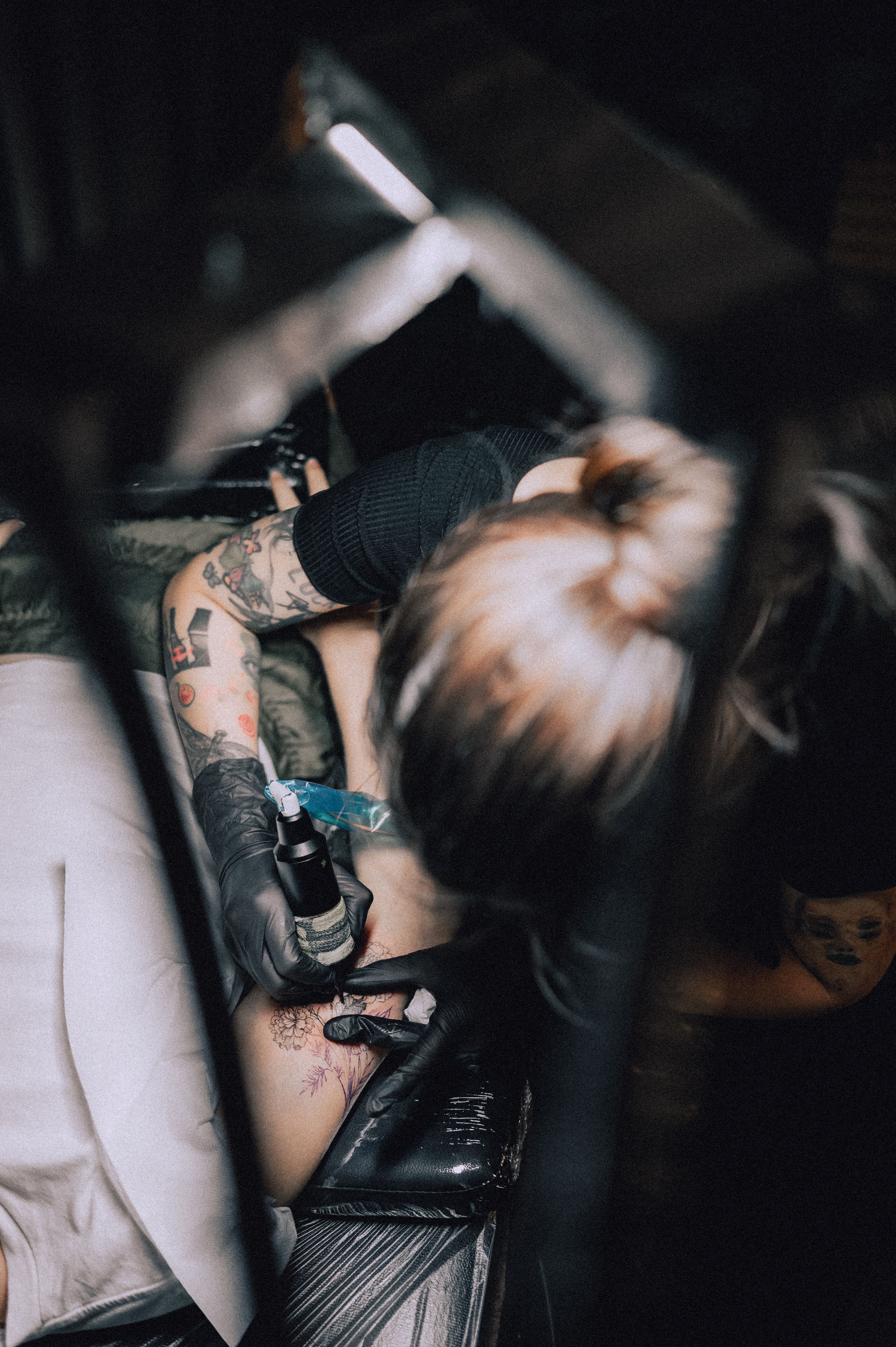 Tatuadora realizando sessão de fine line floral em ângulo dramático